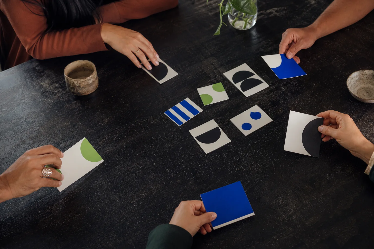 Manos adultas eligiendo tarjetas abstractas de conversación sobre una mesa oscura